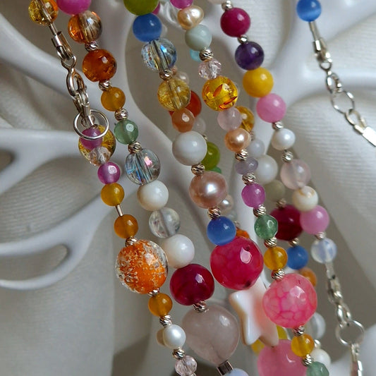 Selection of handcrafted natural semi‑precious gemstone necklaces featuring amethyst, rose quartz, moonstone, lapis lazuli, clear quartz, aquamarine, and green aventurine on a neutral background