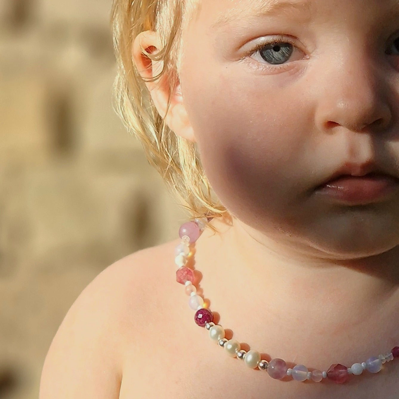 Portrait of a young blonde girl outdoors, showcasing a luxury gemstone necklace featuring ruby, pearls, rose quartz and clear crystal beads