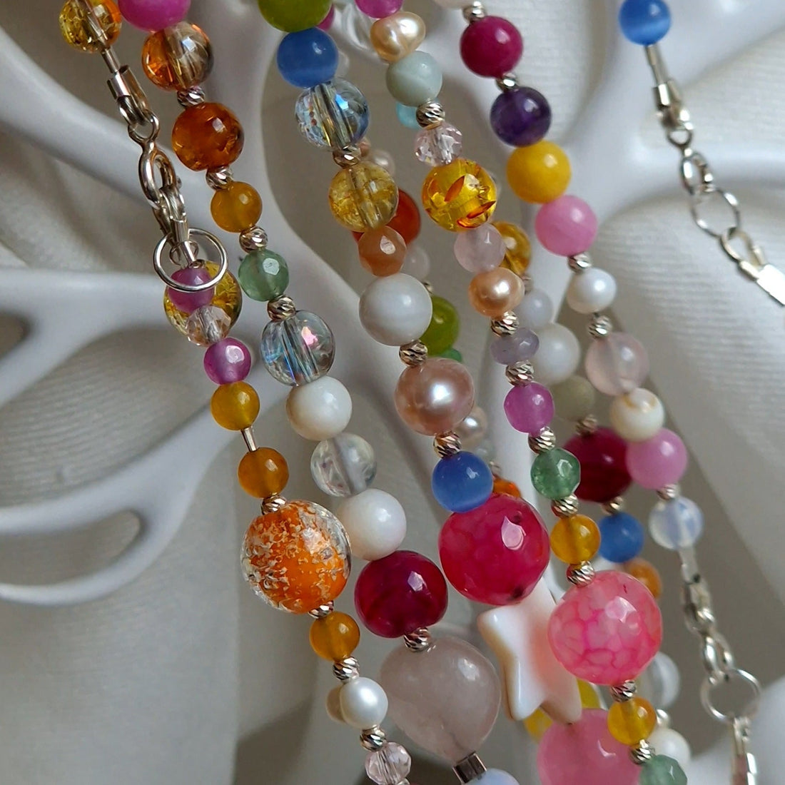 Selection of handcrafted natural semi‑precious gemstone necklaces featuring amethyst, rose quartz, moonstone, lapis lazuli, clear quartz, aquamarine, and green aventurine on a neutral background